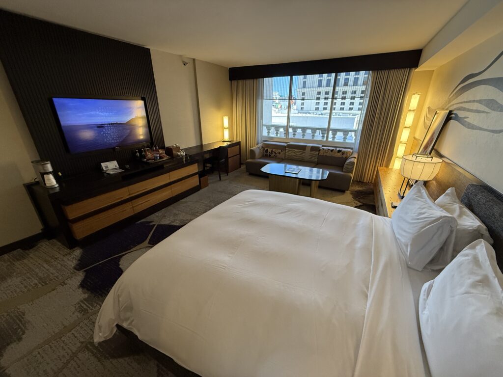 Another angle that shows the king bed pointed at the TV with a couch and window in the background.