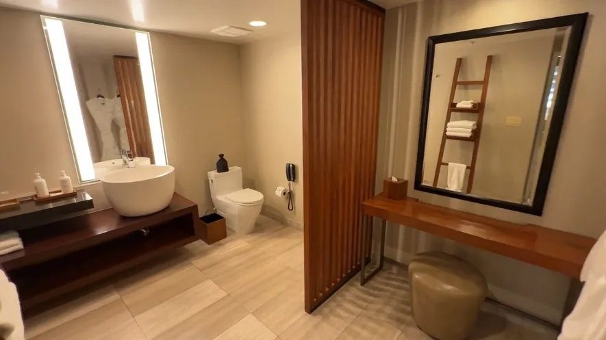on the right, a powder station with a bench, and to the left is the single sink vanity next to a toilet.