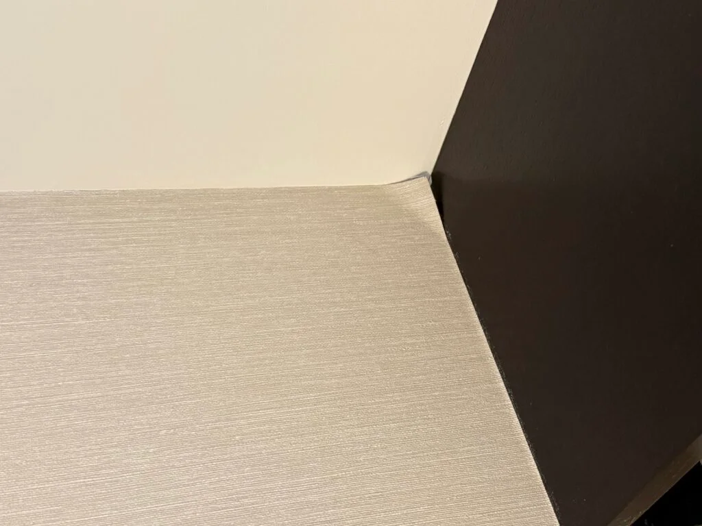 Wallpaper peeling away from the wall in a corner.