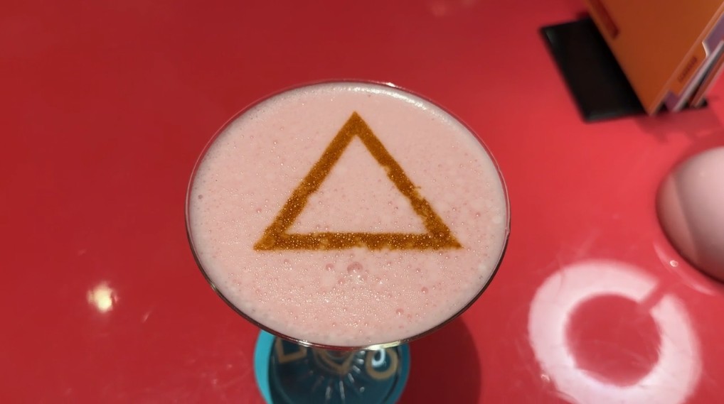 A pink cocktail with a foamy top emblazoned with a triangle.