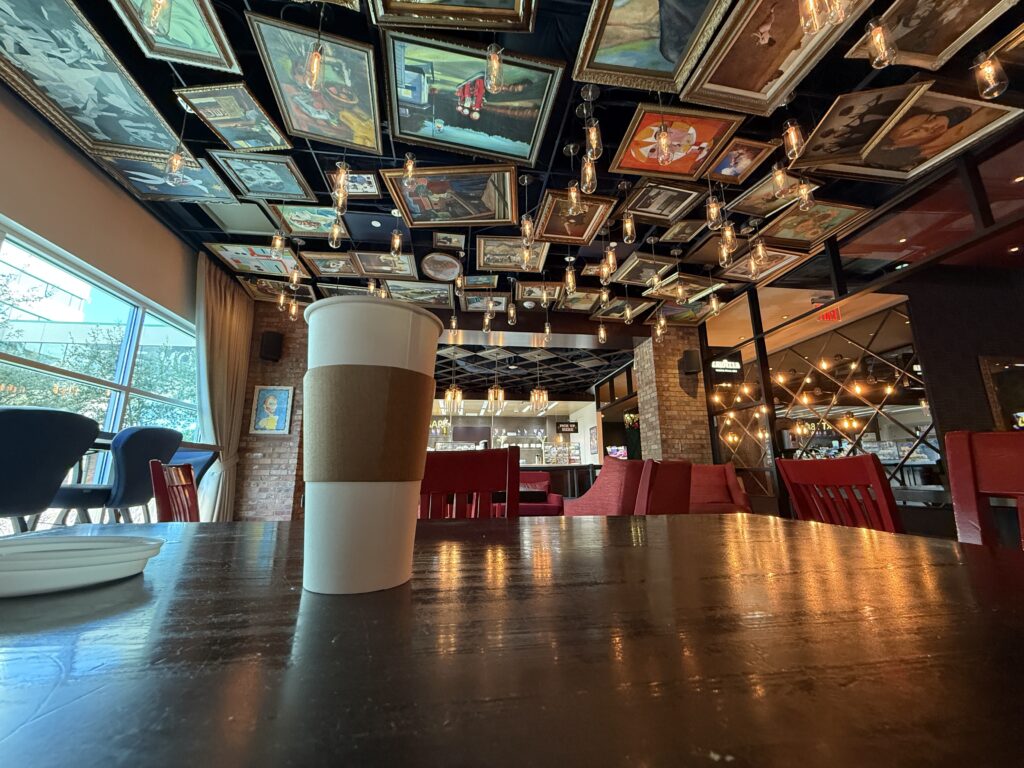 A coffee, sitting on a table, with works of art hanging from the ceiling as decor.