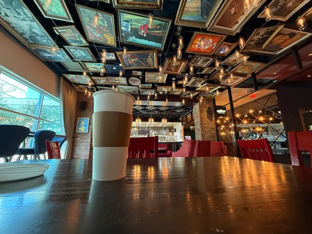 A coffee, sitting on a table, with works of art hanging from the ceiling as decor.