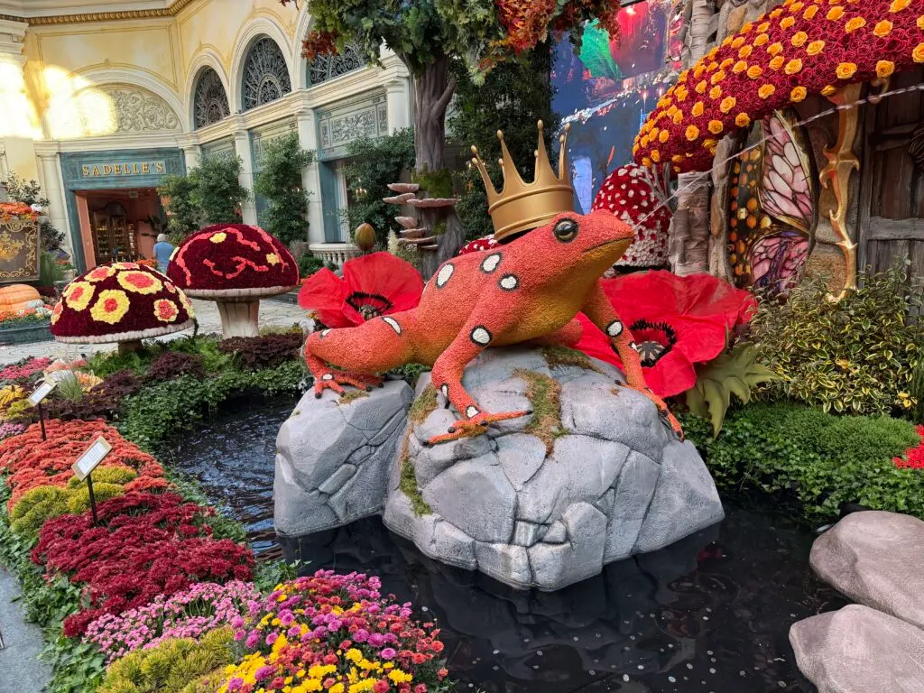 An orange frog, spraying a stream of water from it's mouth while wearing a crown. 