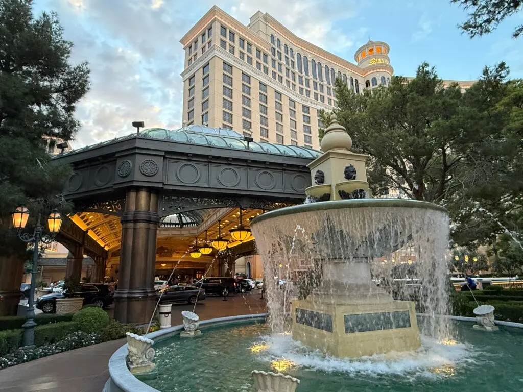 A decorative fountain curns in the foreground, with Bellagio's porte cochere and part of the hotel tower looming behind. 