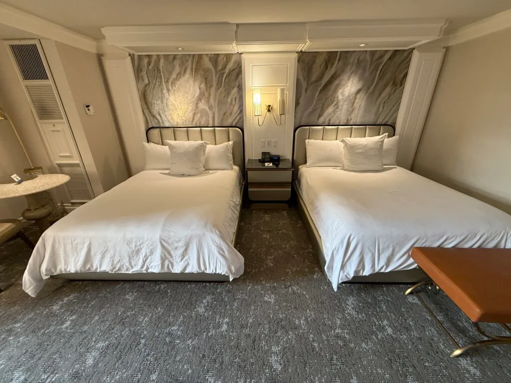 The two queen beds shot head on, one of which has a bench at the end of it. 