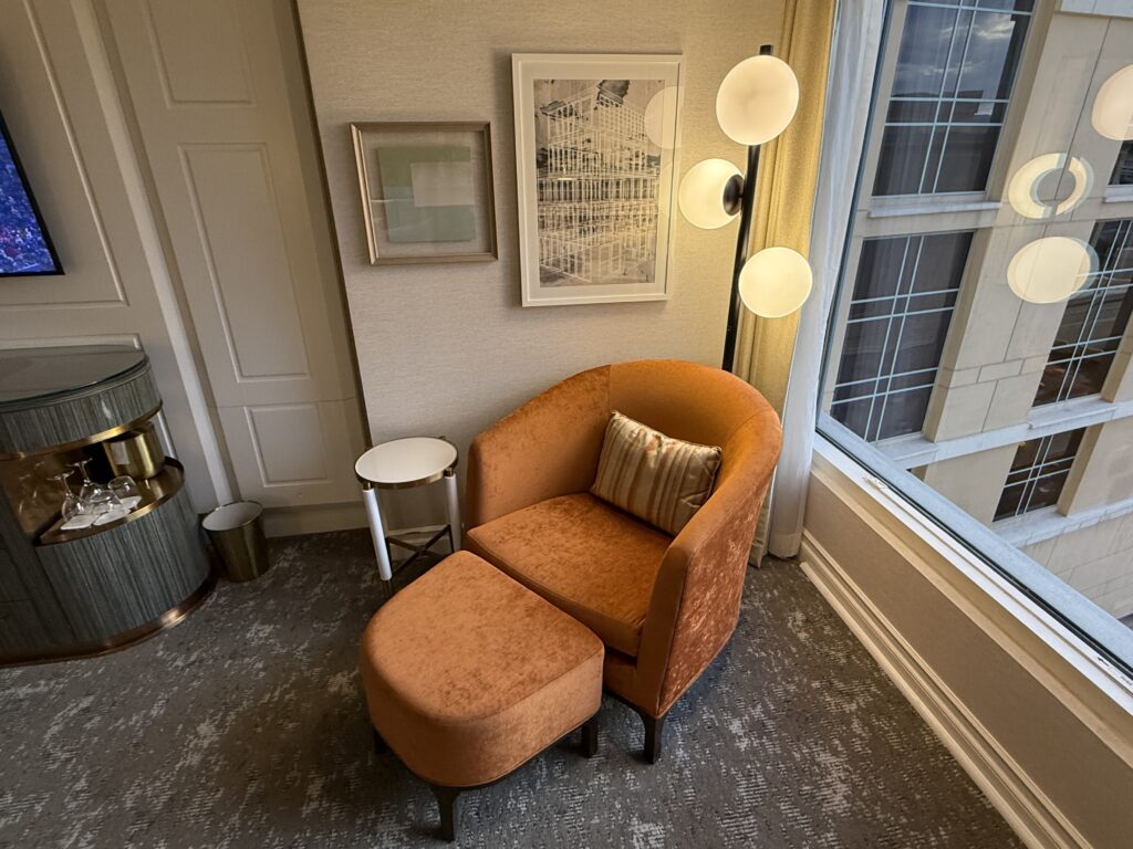 An orange chair and ottoman under a lamp with int's own small circular table next to it.