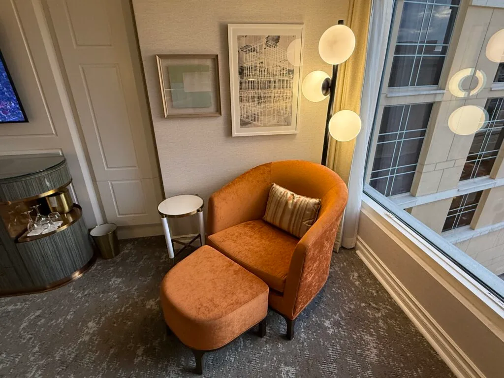 An orange chair and ottoman under a lamp with int's own small circular table next to it. 