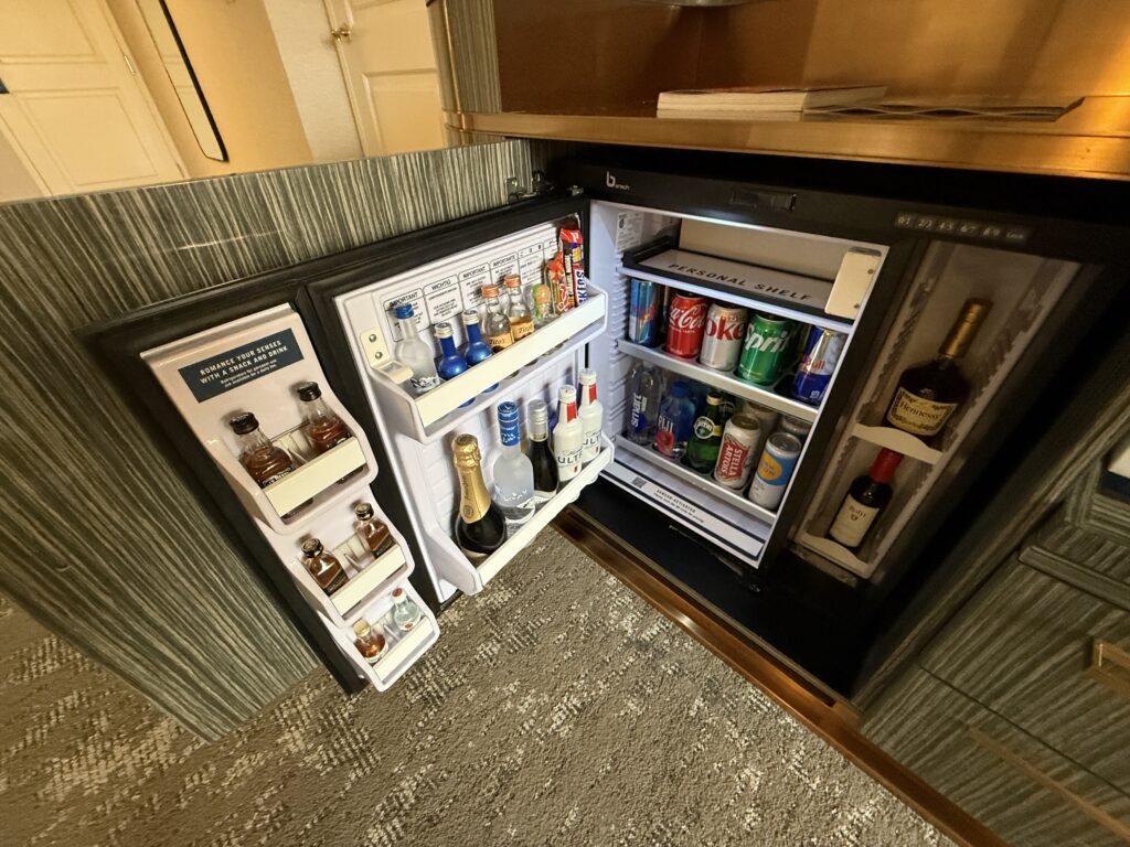An open mini fridge showing beverages for purchase and a small personal shelf.