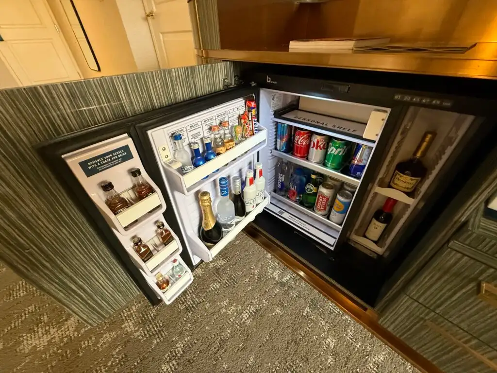 An open mini fridge showing beverages for purchase and a small personal shelf. 