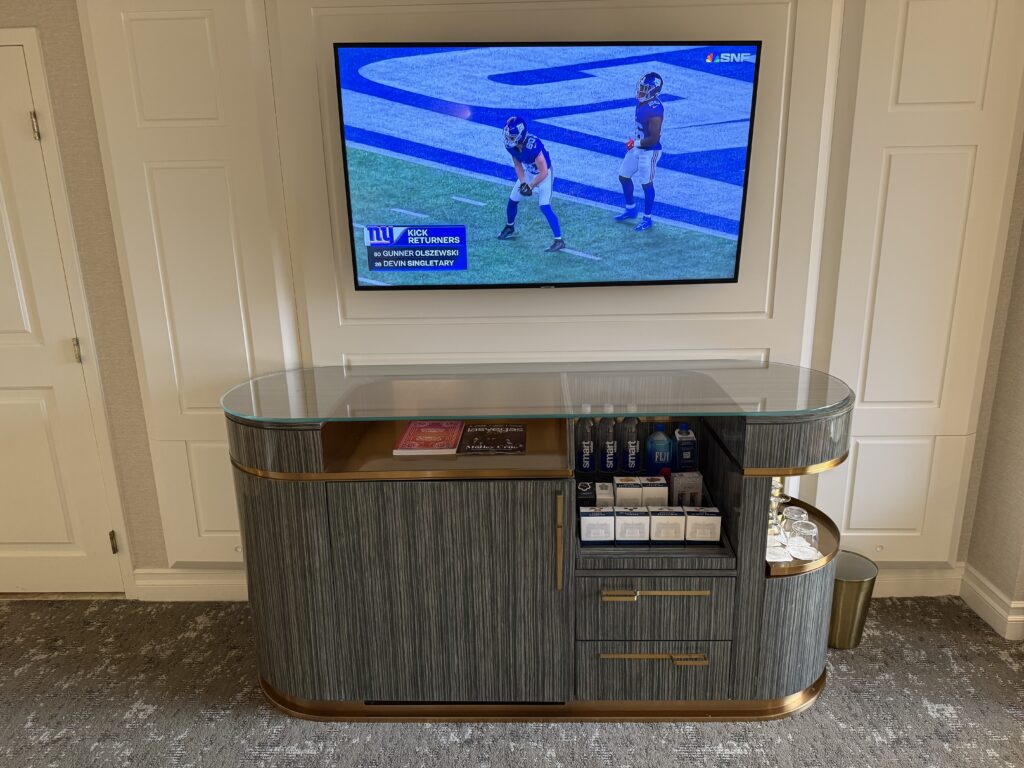 A wall mounted TV above a TV stand wtih dry minibar visible.
