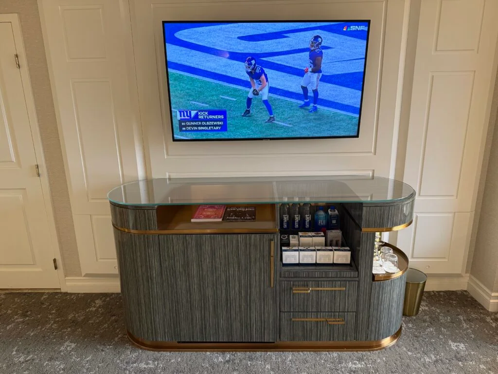A wall mounted TV above a TV stand wtih dry minibar visible. 