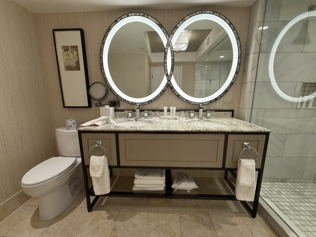 A dual sink vanity topped with an illuminated mirrr wihch appears to combine two circular mirrors into one.