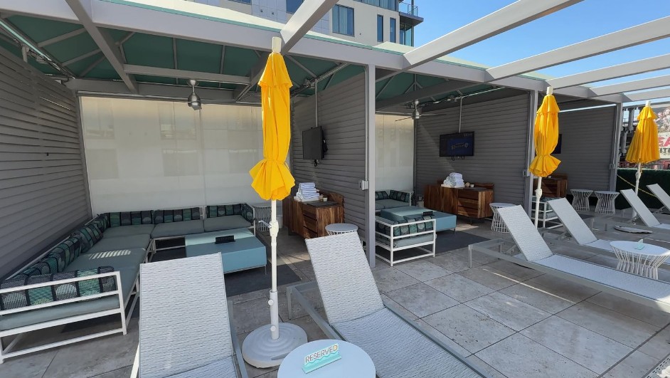 A row of cabanas, with yellow unbrellas, loungers, and TVs mounted on the wall.