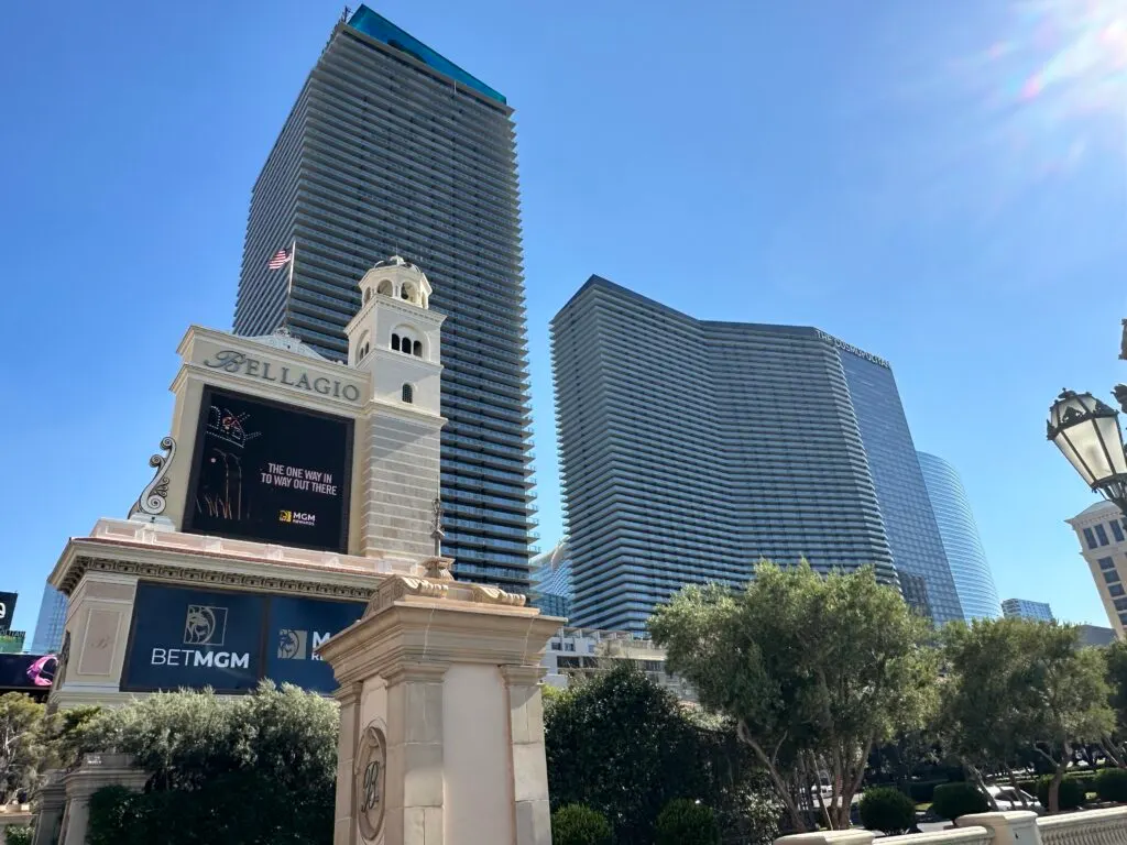 Exterior of Cosmopolitan's 2 towers with a blue sky behind and a giant Bellagio sign in the foreground.