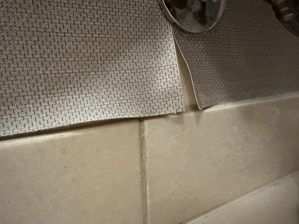 Peeling wallpaper behind the toilet.