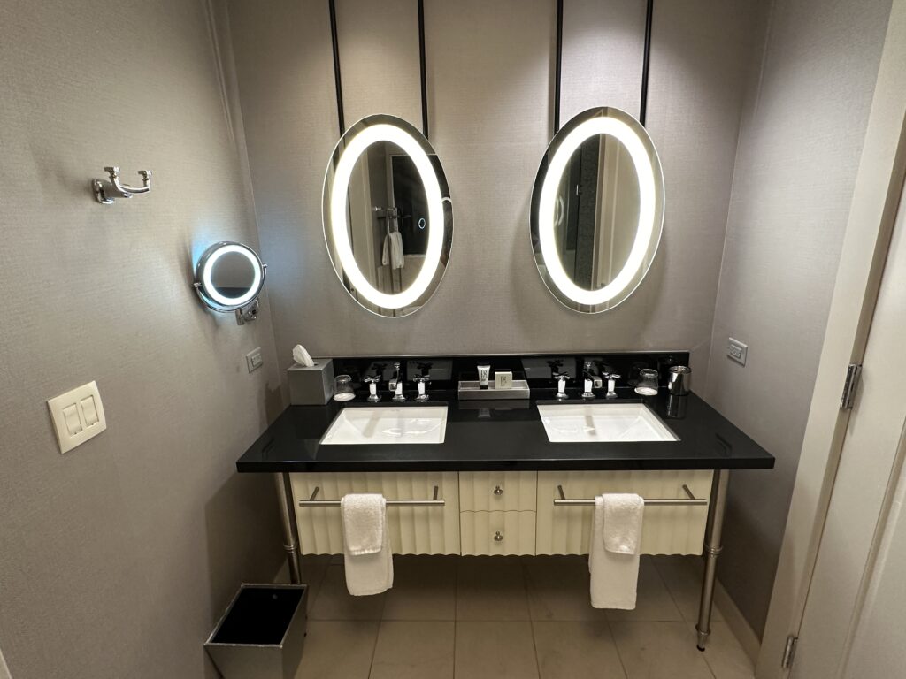 A dual sink vanity, topped with two separate illuminated mirrors in the shape of an oval.
