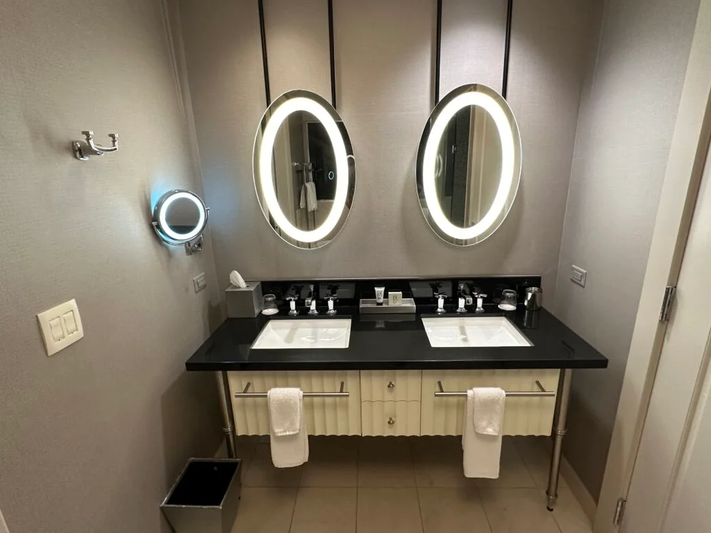 A dual sink vanity, topped with two separate illuminated mirrors in the shape of an oval. 