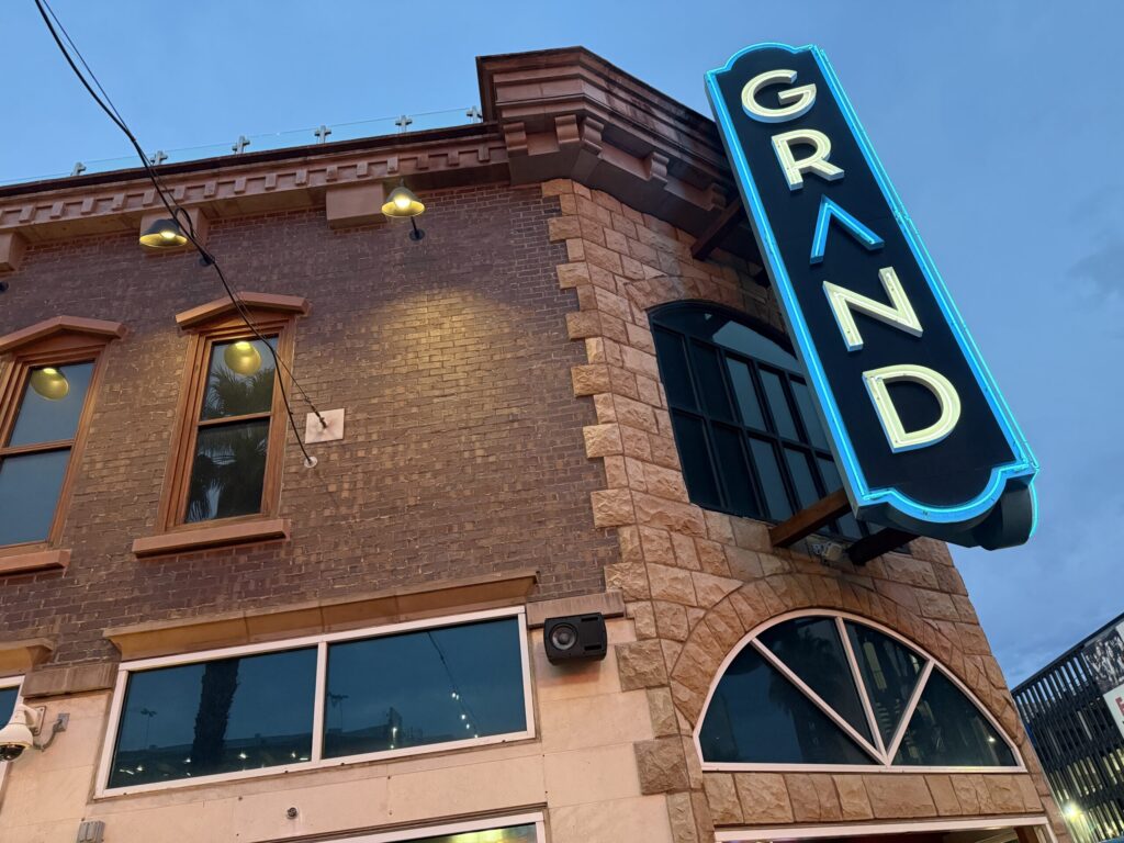 A neon sign, posted on the exterior of the building that says "GRAND".