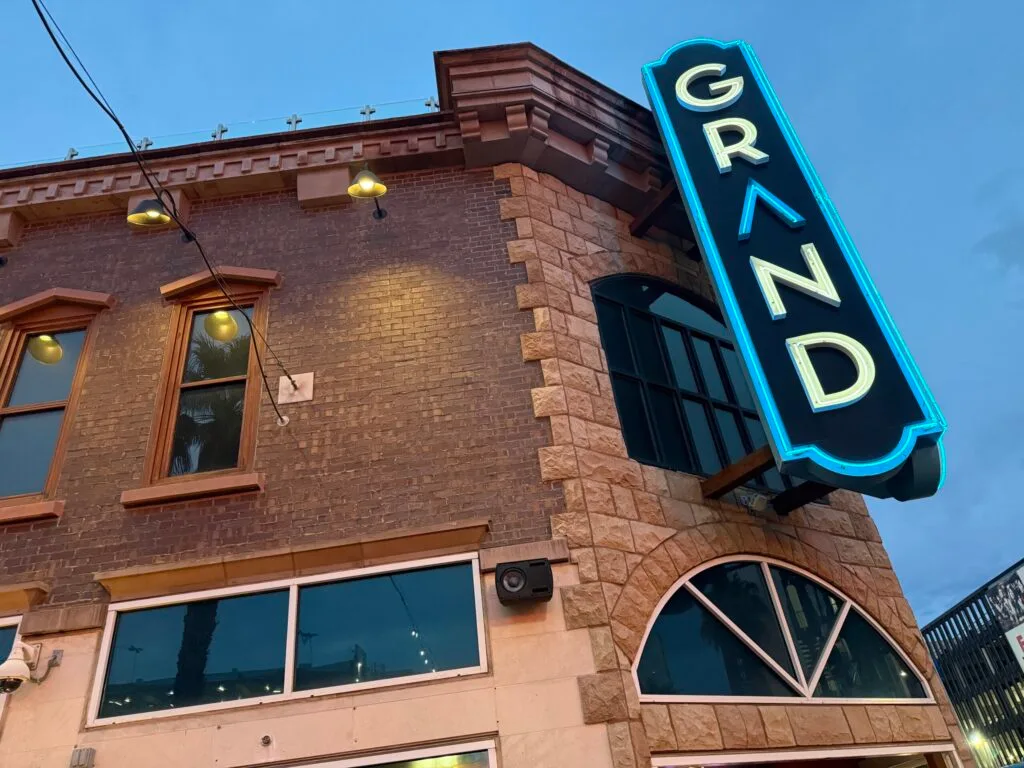 A neon sign, posted on the exterior of the building that says "GRAND".