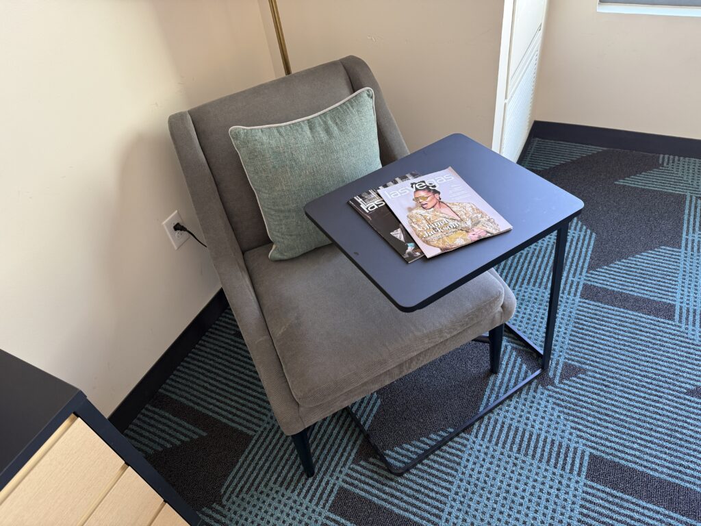 A chair in the corner with a table nested over it. On the table are two Las Vegas magazines.