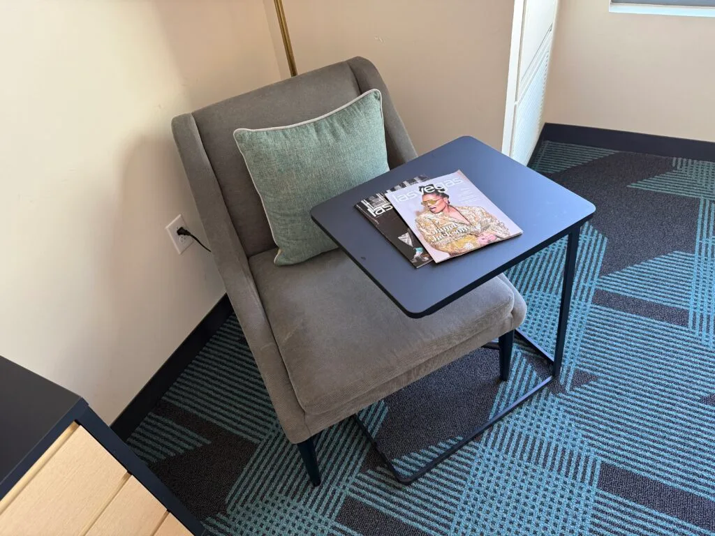 A chair in the corner with a table nested over it. On the table are two Las Vegas magazines. 