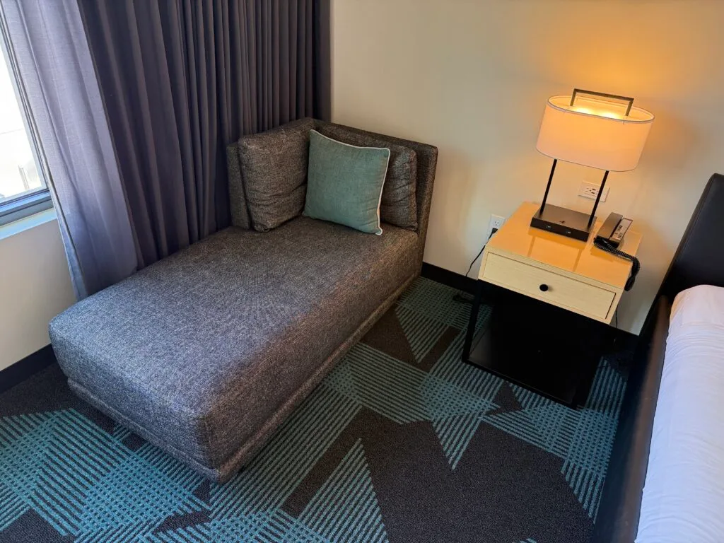 A small couch in the corner, with one decoratove pillow on it. 