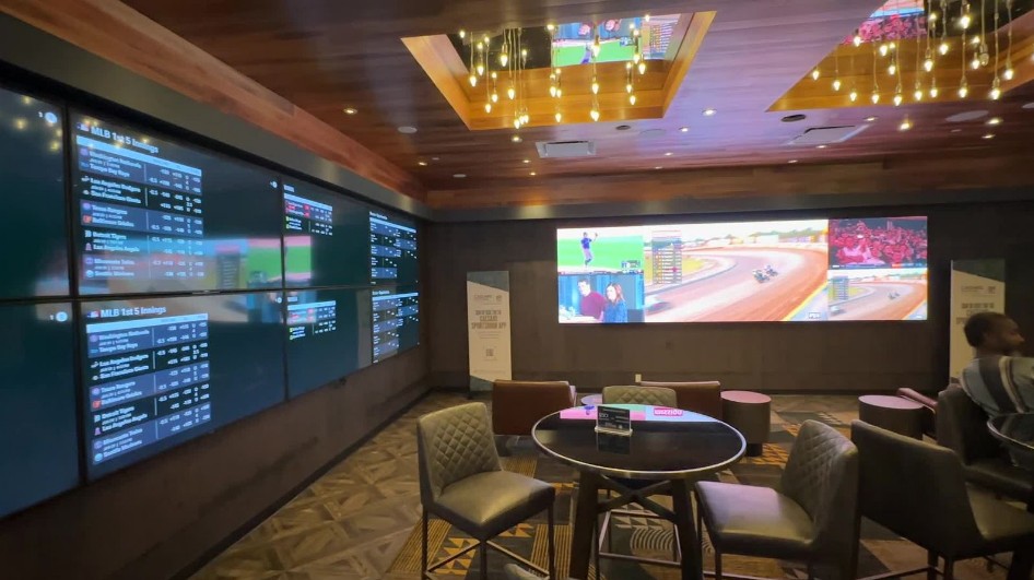 A small sportsbook, with a video wall and odds posted on another. Seating is limited.