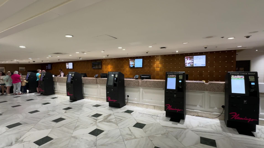 A bank of self check in kiosks stand vacant in front of the lobby desk.