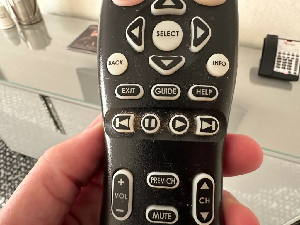 A remote control with lint and dust around the buttons. 