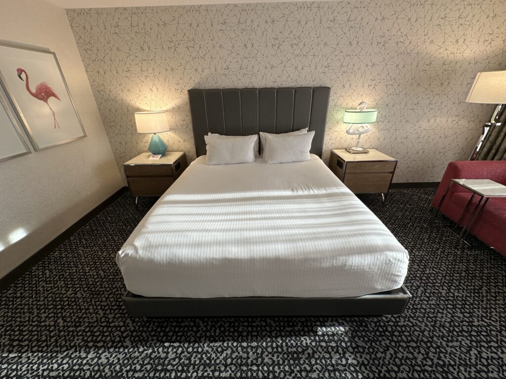 A head on shot of the bed, from the foot of it. The bed is flanked by end tables, one of which has a lamp in the shape of a flamingo.