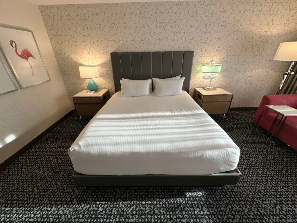 A head on shot of the bed, from the foot of it. The bed is flanked by end tables, one of which has a lamp in the shape of a flamingo. 