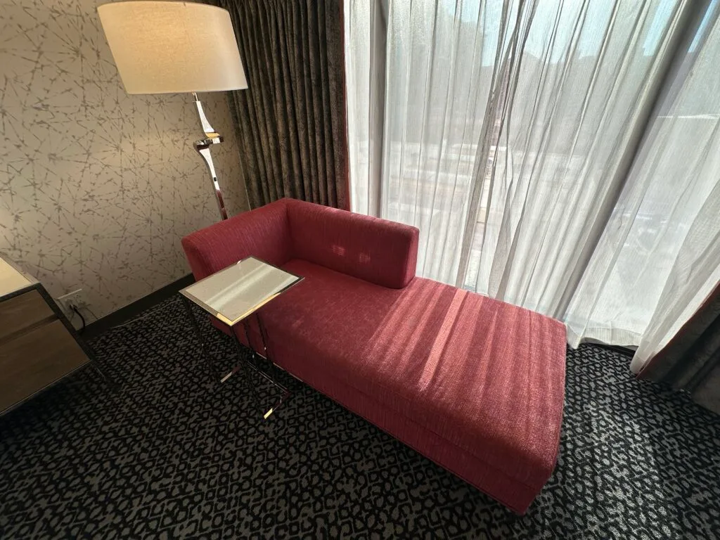 A pink couch with a little built in table up against the window. 