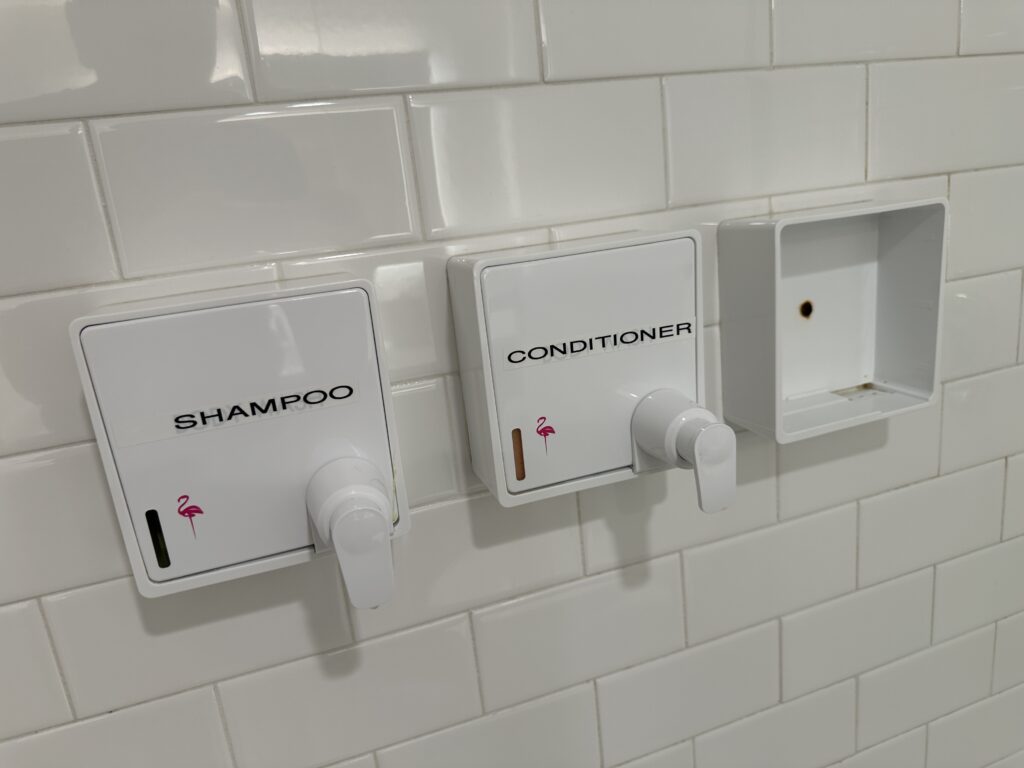 An empty toiletry dispenser shell in the shower.