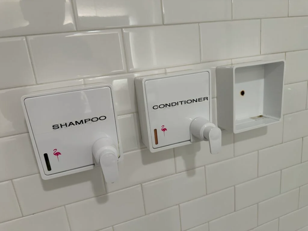 An empty toiletry dispenser shell in the shower. 