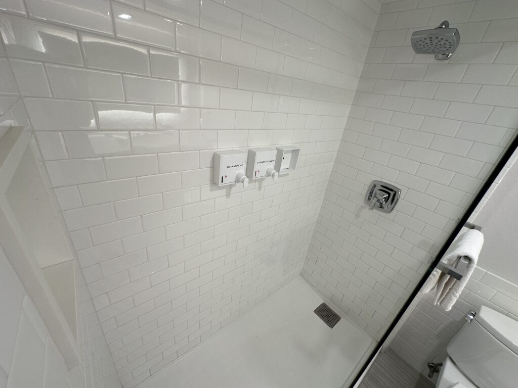 A shower, with a half glass partitian and white subway tile walls.