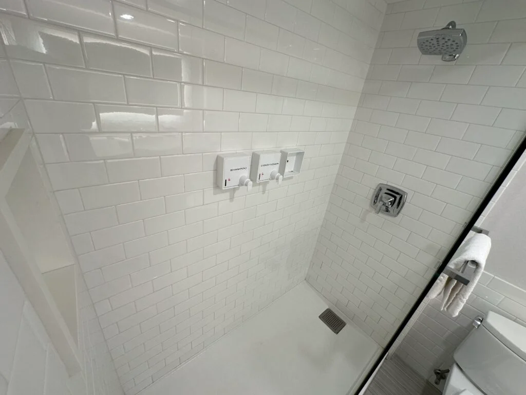 A shower, with a half glass partitian and  white subway tile walls. 
