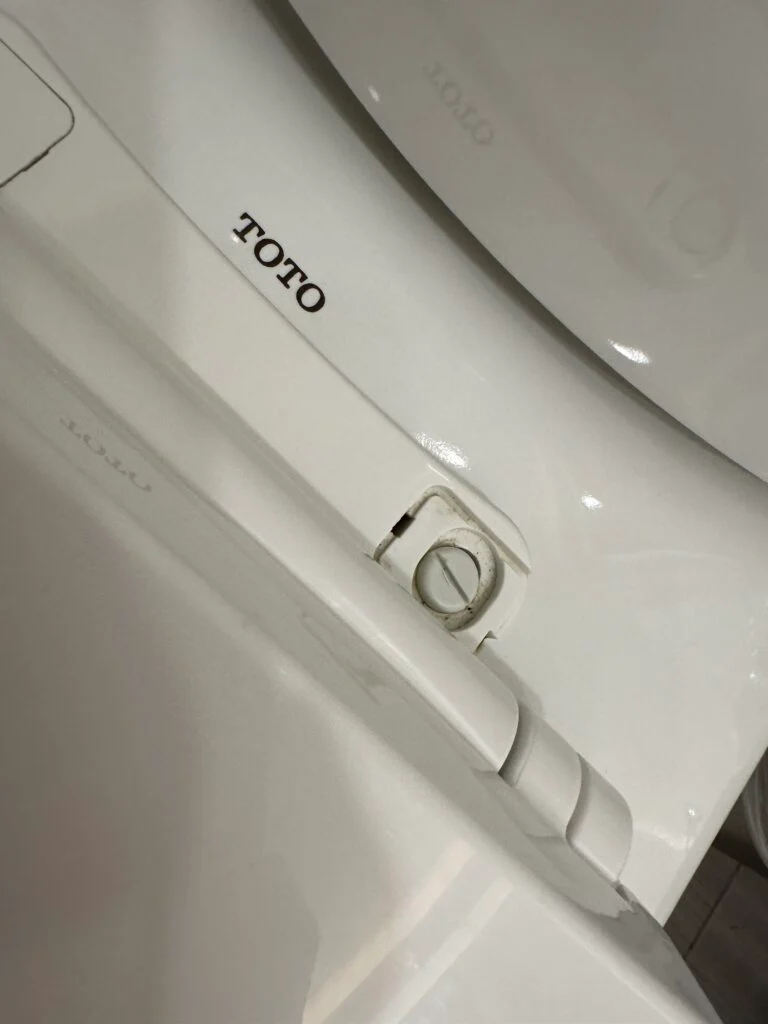 A toilet seat, with one screw missing its decorative cap. 