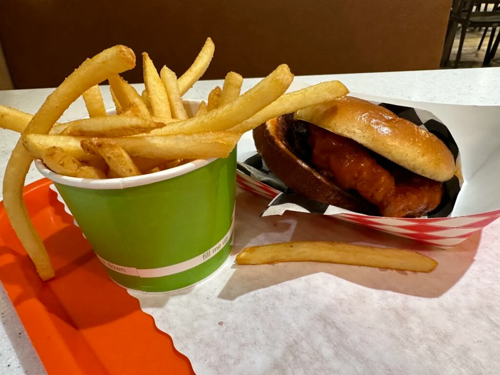 A chicken sandwich, sitting next to a cup of french fries. 