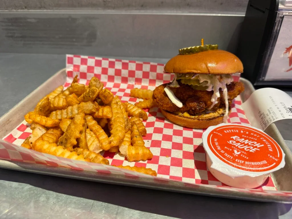 A chicken sandwich on a tray next to a pile of french fries. 