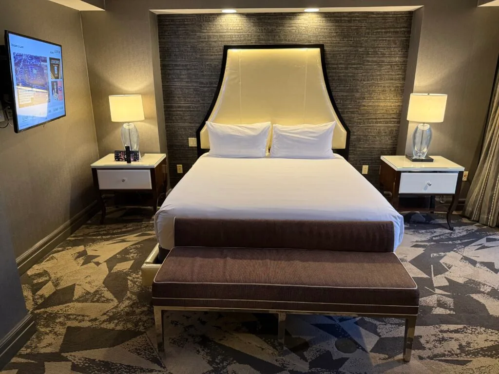 Head on shot of the king bed, with a bench at the end, and flanked by end tables that demonstrates the weird TV angle. 