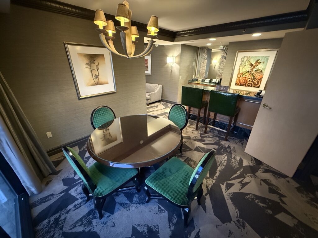 A circle table, with 4 emerald green chairs around it. A 2 seat bar is in the background.