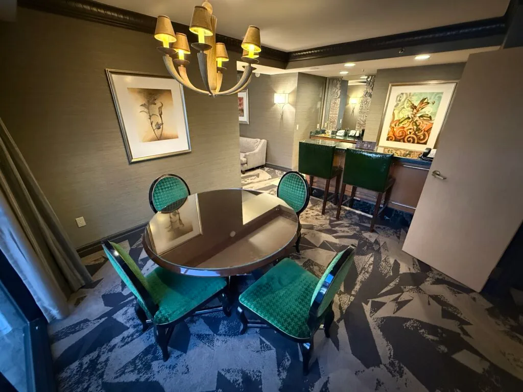 A circle table, with 4 emerald green chairs around it. A 2 seat bar is in the background. 