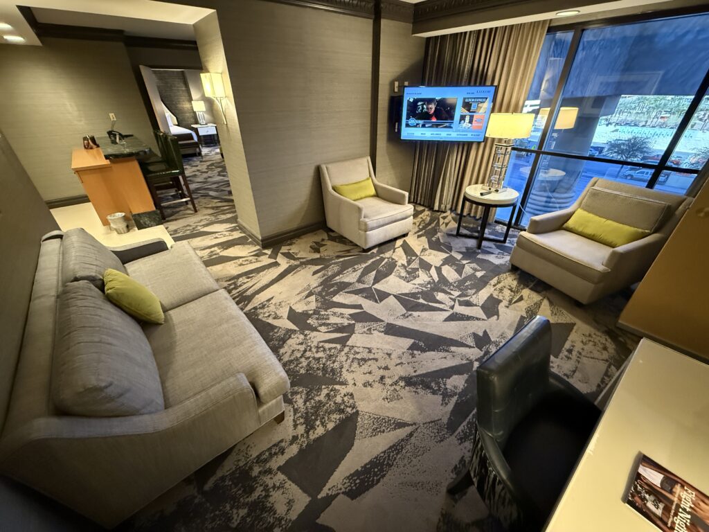Wide angle view of the living area, including a couch, 2 chairs, and a workdesk.