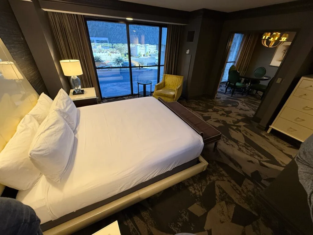 Another view of the room, which shoes the king bed in the foreground, windows in the background and a doorway to the dining area to the right. 
