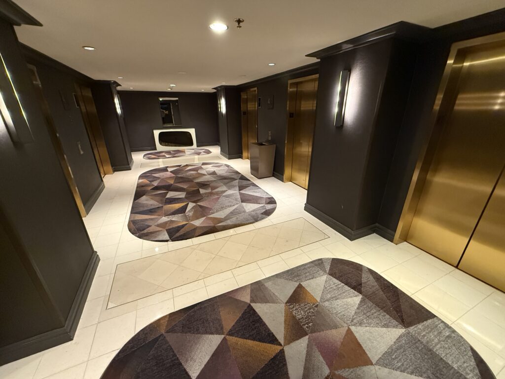 Brass elevator doors, dark wood, and carpet with triangles on it - The elevator lobby looks borderline nice.
