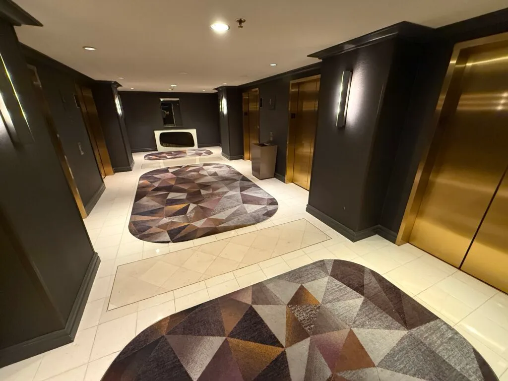 Brass elevator doors, dark wood, and carpet with triangles on it - The elevator lobby looks borderline nice. 