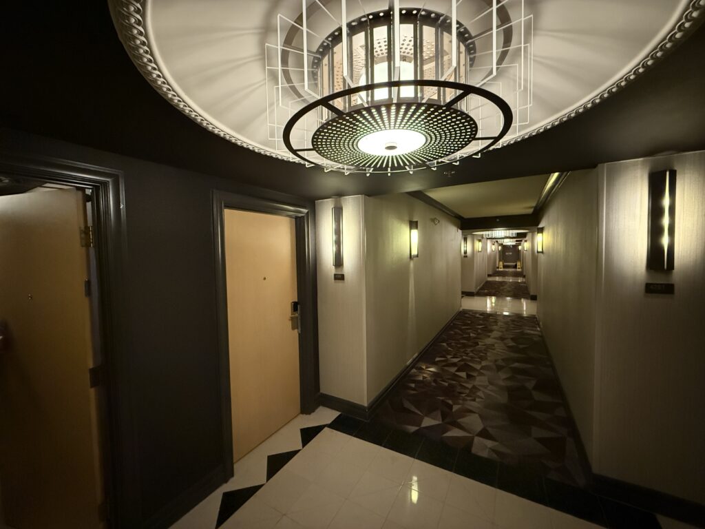 A decorative chandelier hanging above the hotel hallway. In the distance you can see a couple of wet floor signs.
