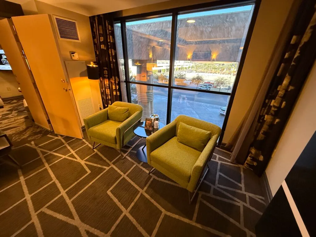 Two green chairs with a small table between them in front of the window.