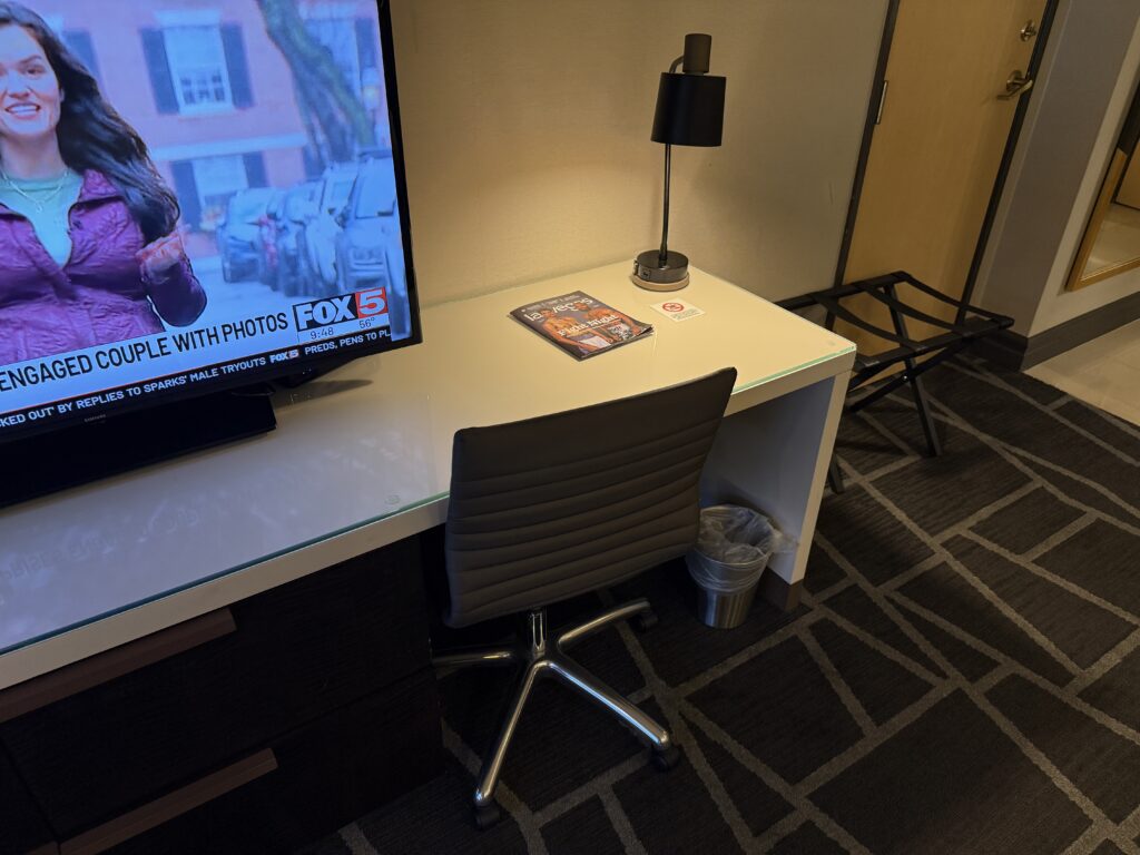 A very small workdesk which is being crowded out by the TV.