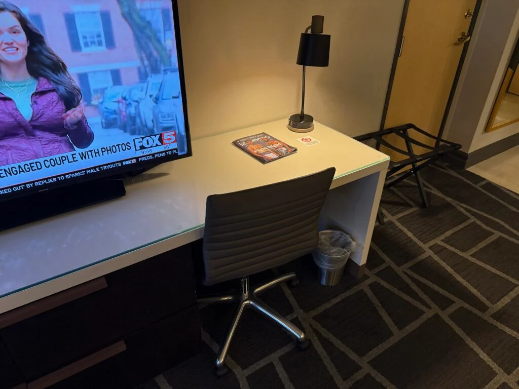 A very small workdesk which is being crowded out by the TV.